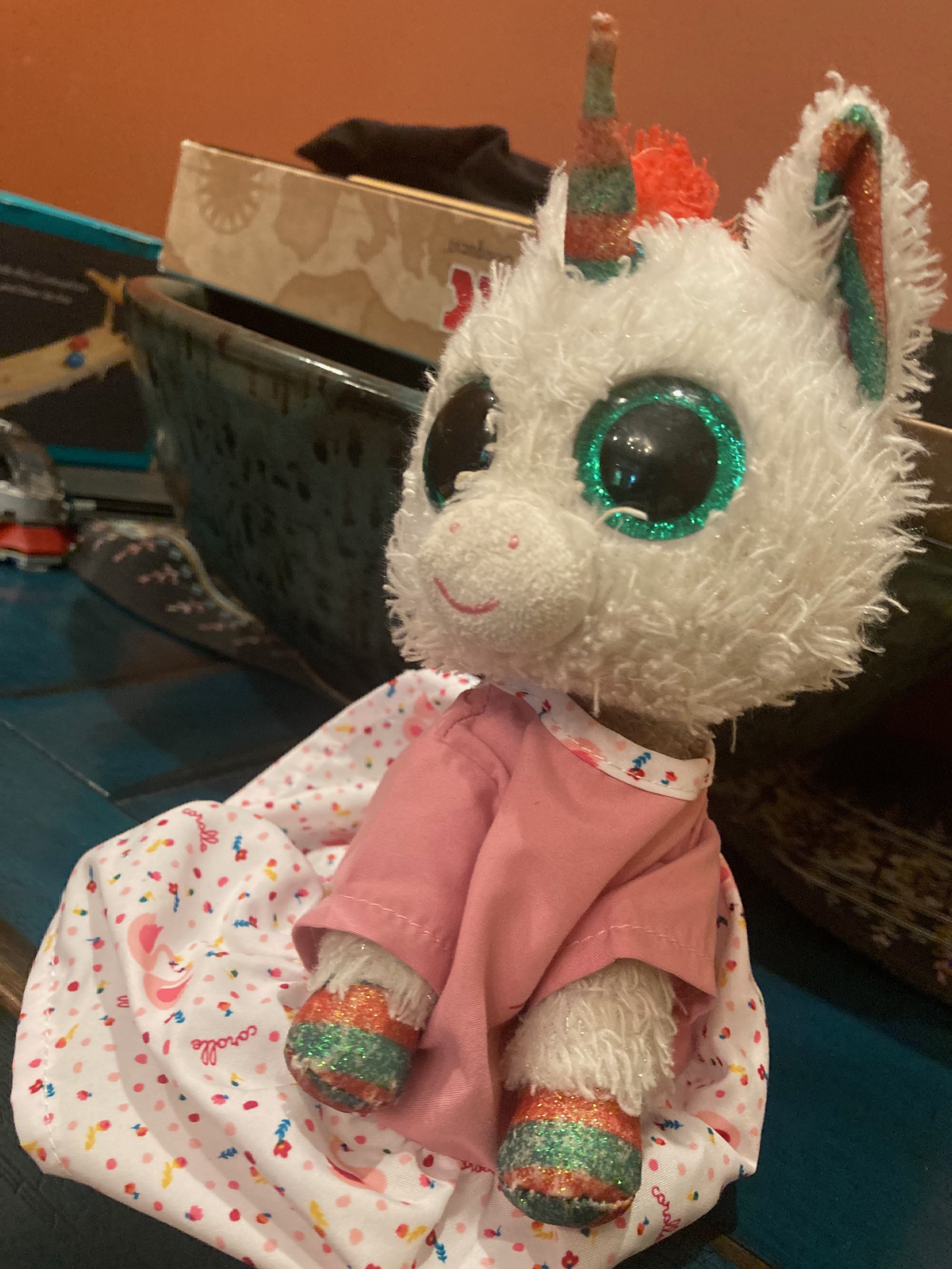 A stuffed toy unicorn with red and green hooves wearing a pink dress.